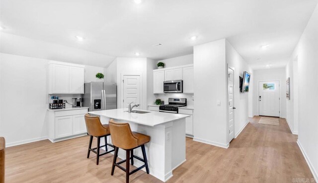 kitchen with appliances with stainless steel finishes, a kitchen island with sink, sink, white cabinets, and a breakfast bar area