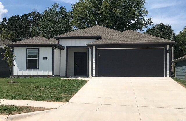 view of front of house with a front lawn, board and batten siding, an attached garage, and a shingled roof