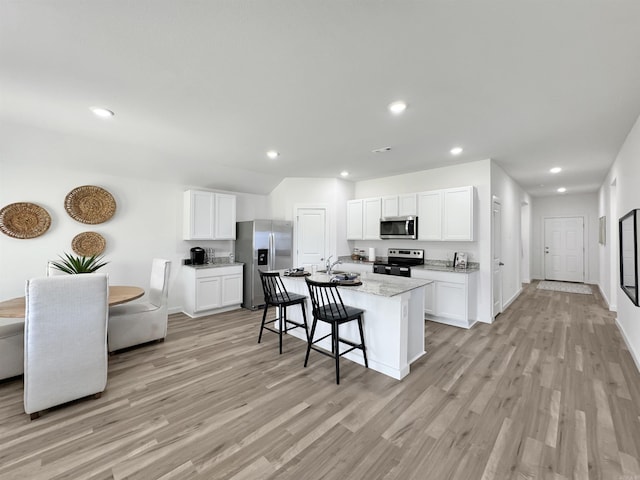 kitchen featuring white cabinets, appliances with stainless steel finishes, a center island with sink, and light stone counters