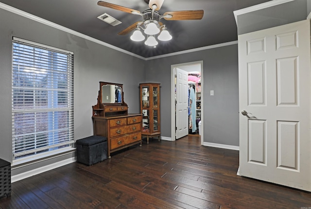 interior space featuring a walk in closet, ceiling fan, crown molding, dark hardwood / wood-style floors, and a closet