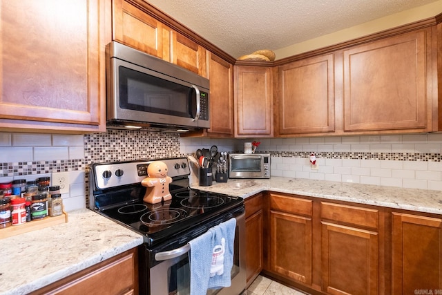 kitchen featuring a textured ceiling, backsplash, stainless steel appliances, and light stone counters