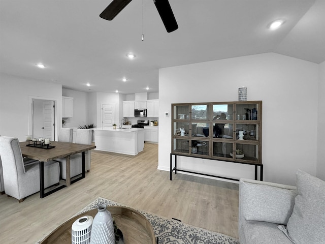 living room with ceiling fan, light hardwood / wood-style floors, sink, and vaulted ceiling