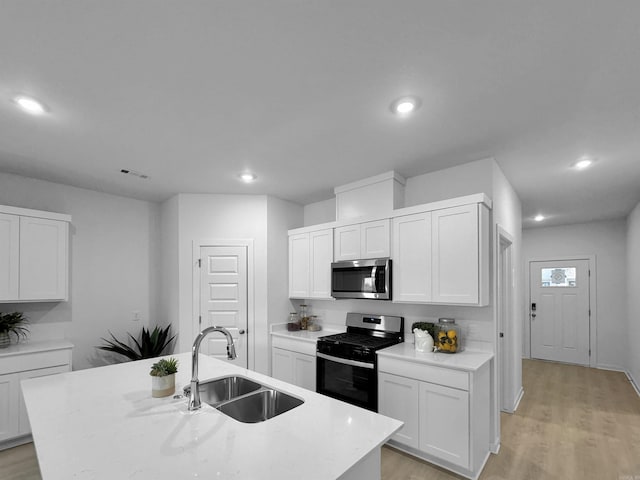 kitchen featuring sink, stainless steel appliances, a kitchen island with sink, white cabinets, and light wood-type flooring