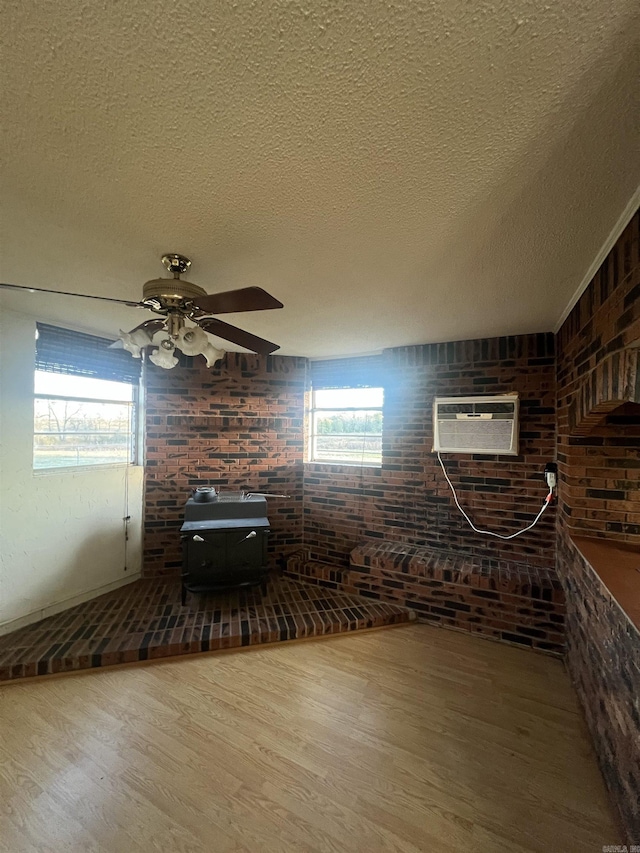 interior space featuring ceiling fan, an AC wall unit, hardwood / wood-style flooring, a textured ceiling, and brick wall