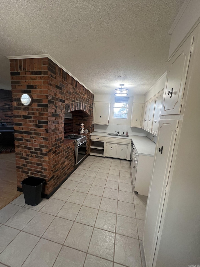 kitchen featuring light tile patterned flooring, a textured ceiling, range, white cabinets, and sink