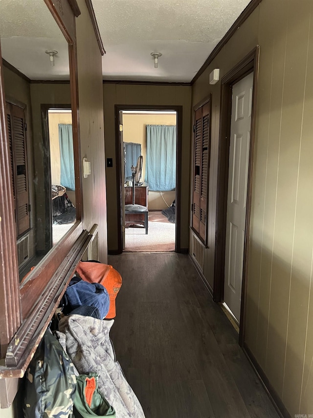 corridor featuring wooden walls, ornamental molding, dark hardwood / wood-style floors, and a textured ceiling