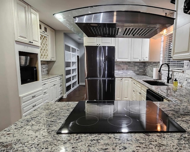 kitchen featuring black appliances, island range hood, light stone counters, and sink