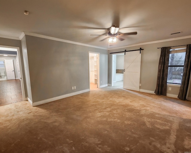 carpeted empty room featuring a barn door, ceiling fan, and ornamental molding