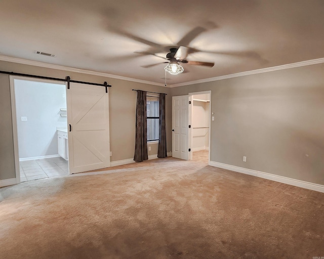 unfurnished bedroom with light carpet, ensuite bath, ceiling fan, crown molding, and a barn door