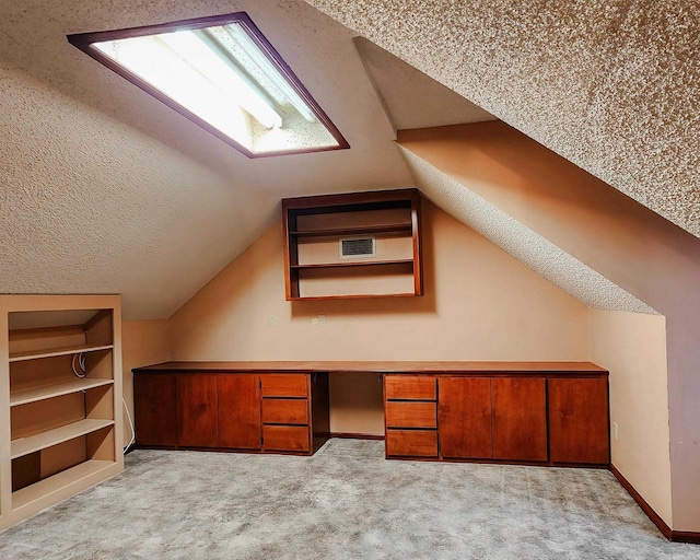 additional living space featuring built in shelves, light colored carpet, built in desk, and vaulted ceiling