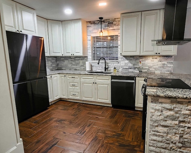 kitchen with sink, hanging light fixtures, wall chimney range hood, light stone counters, and fridge