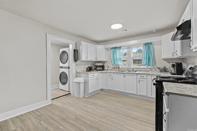 kitchen with sink, stainless steel range with electric cooktop, ventilation hood, stacked washer and dryer, and white cabinets