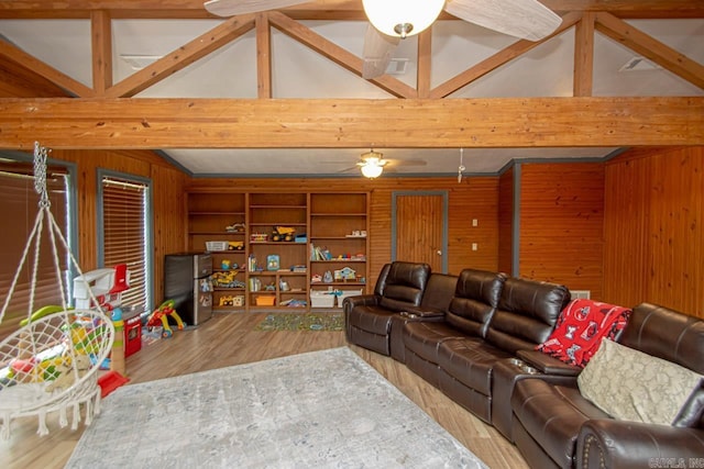 living room with hardwood / wood-style floors, wooden walls, built in shelves, ceiling fan, and vaulted ceiling with beams