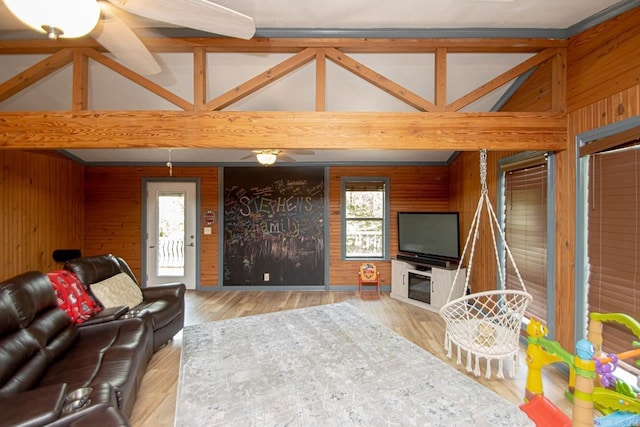 living room featuring vaulted ceiling with beams, wood walls, light wood-type flooring, and ceiling fan