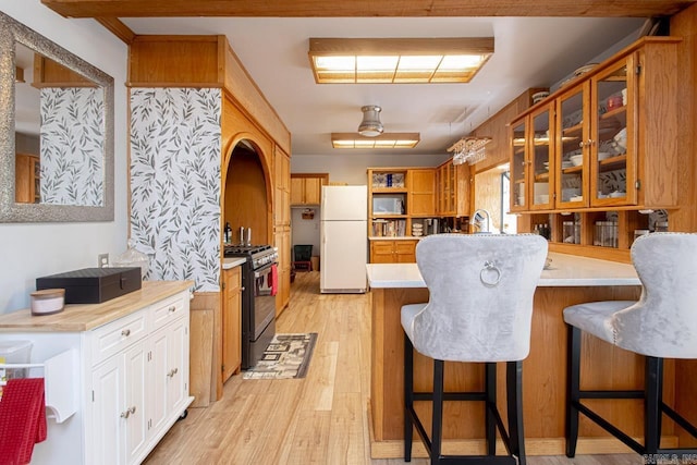 kitchen featuring high end range, kitchen peninsula, light hardwood / wood-style flooring, white fridge, and a breakfast bar area