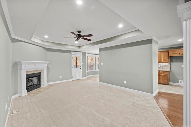 unfurnished living room featuring ceiling fan, a raised ceiling, ornamental molding, and light hardwood / wood-style flooring