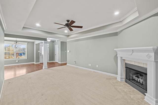 unfurnished living room featuring a raised ceiling, light colored carpet, a tiled fireplace, ceiling fan with notable chandelier, and ornamental molding