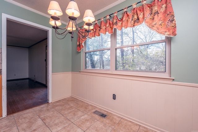 unfurnished dining area with tile patterned flooring, ornamental molding, and an inviting chandelier