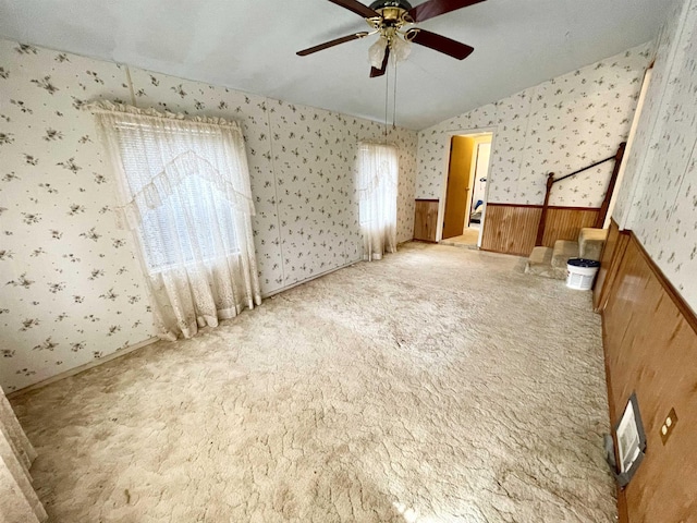 carpeted spare room featuring ceiling fan, lofted ceiling, and wood walls