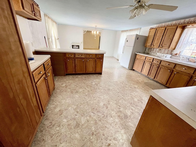 kitchen with ceiling fan with notable chandelier, white refrigerator, kitchen peninsula, and hanging light fixtures