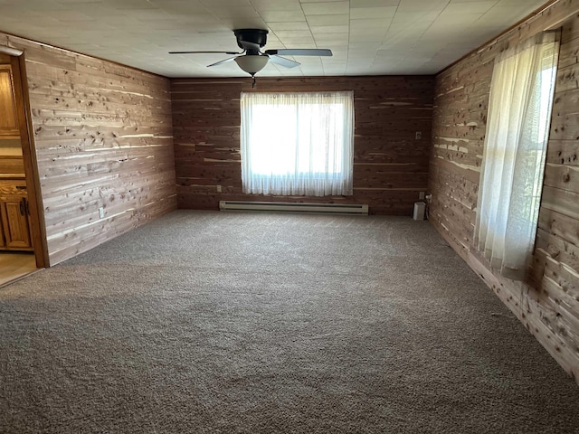 carpeted empty room with ceiling fan, a healthy amount of sunlight, wooden walls, and a baseboard heating unit