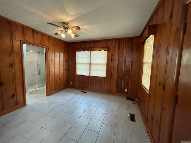 unfurnished bedroom featuring ensuite bath, ceiling fan, crown molding, and wooden walls