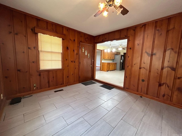 empty room featuring ceiling fan with notable chandelier and wood walls