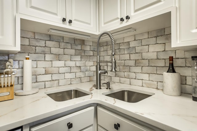 kitchen featuring light stone countertops, tasteful backsplash, white cabinetry, and sink