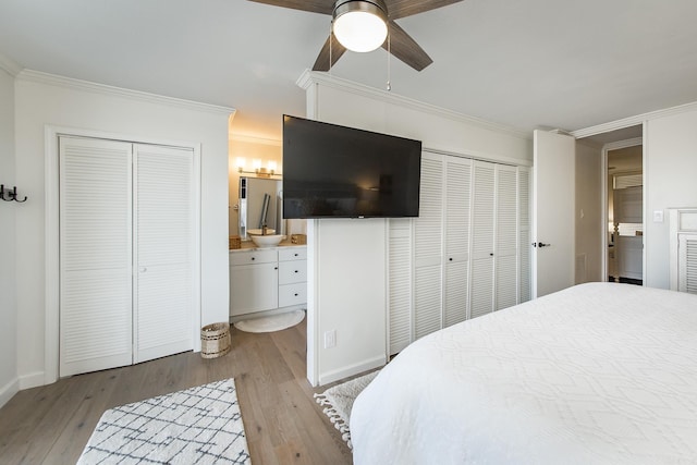 bedroom featuring light wood-type flooring, ornamental molding, two closets, ceiling fan, and connected bathroom