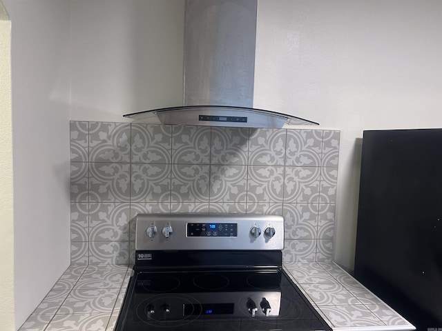 kitchen featuring decorative backsplash, black fridge, stainless steel range with electric cooktop, and exhaust hood