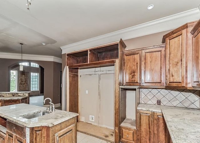 kitchen with light stone countertops, sink, backsplash, a center island with sink, and ornamental molding