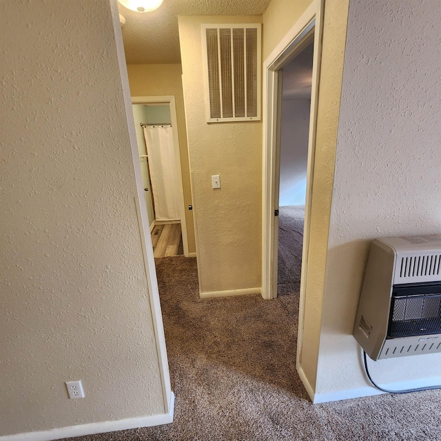 hallway featuring a textured ceiling, carpet floors, and heating unit