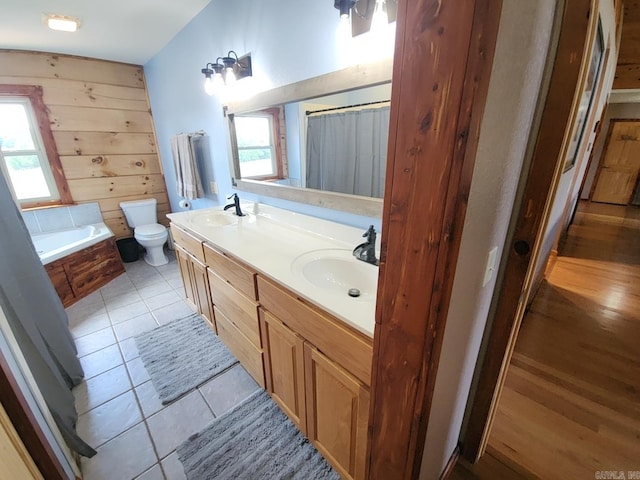 bathroom with tile patterned flooring, a bath, wood walls, toilet, and vanity