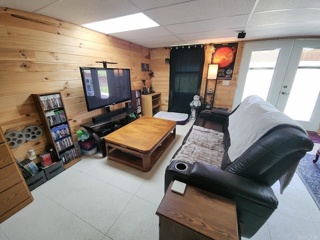 living room featuring french doors, a drop ceiling, and wood walls