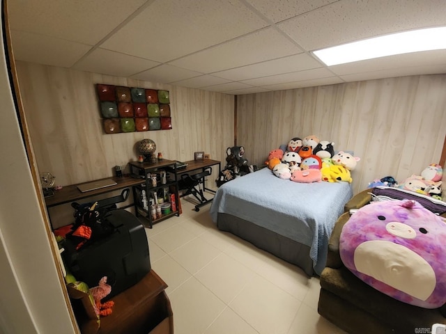 bedroom featuring light tile patterned floors, a drop ceiling, and wood walls