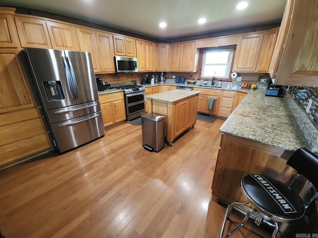 kitchen featuring a center island, backsplash, light hardwood / wood-style flooring, light stone counters, and stainless steel appliances