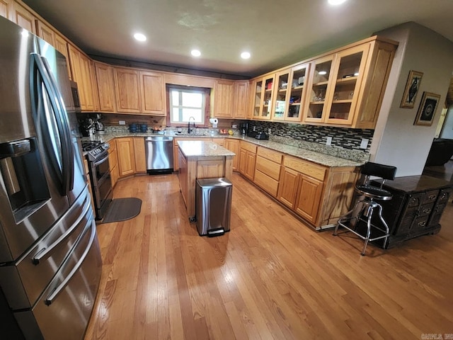 kitchen featuring light stone countertops, light hardwood / wood-style floors, a breakfast bar, a kitchen island, and appliances with stainless steel finishes