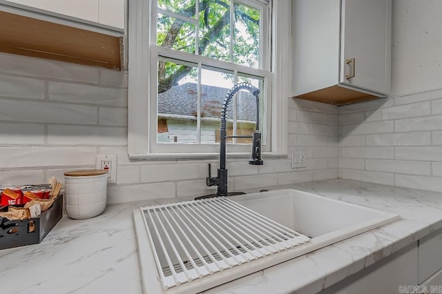 details featuring tasteful backsplash, white cabinets, light stone countertops, and sink