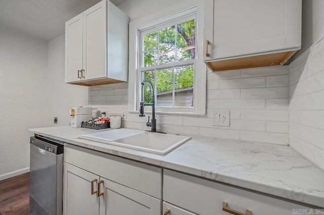 kitchen with decorative backsplash, stainless steel dishwasher, white cabinets, light stone counters, and sink