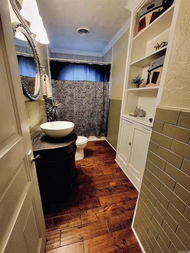 bathroom with hardwood / wood-style floors, toilet, vanity, tile walls, and ornamental molding