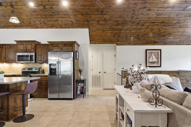 kitchen featuring tasteful backsplash, dark brown cabinetry, stainless steel appliances, hanging light fixtures, and light tile patterned flooring