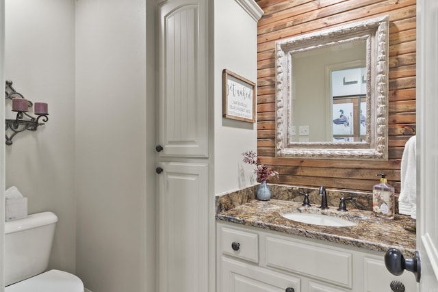 bathroom with vanity, toilet, and wooden walls