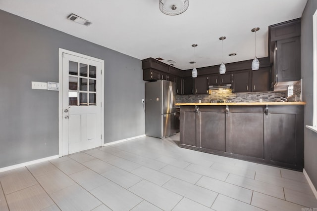 kitchen featuring kitchen peninsula, stainless steel fridge, decorative light fixtures, decorative backsplash, and a breakfast bar