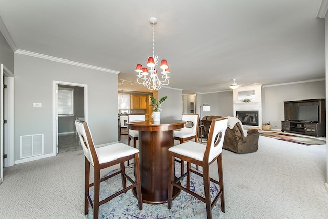 dining room with crown molding, a large fireplace, light colored carpet, and a notable chandelier