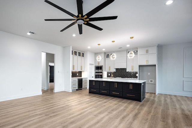 kitchen featuring stainless steel microwave, a center island with sink, white cabinetry, and hanging light fixtures