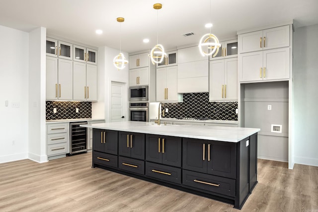 kitchen featuring pendant lighting, a center island with sink, white cabinetry, stainless steel appliances, and beverage cooler