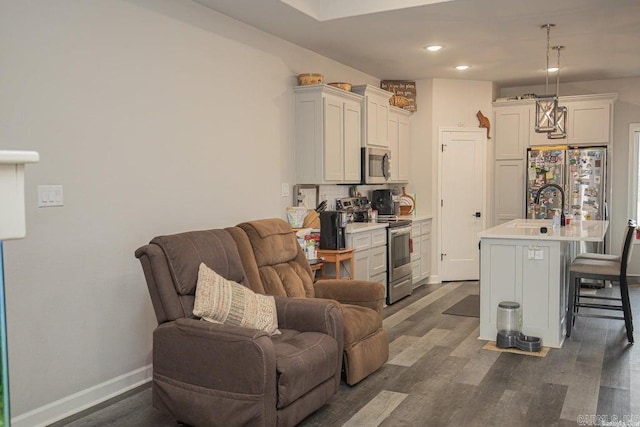 kitchen featuring appliances with stainless steel finishes, dark hardwood / wood-style flooring, a breakfast bar, decorative light fixtures, and a center island with sink