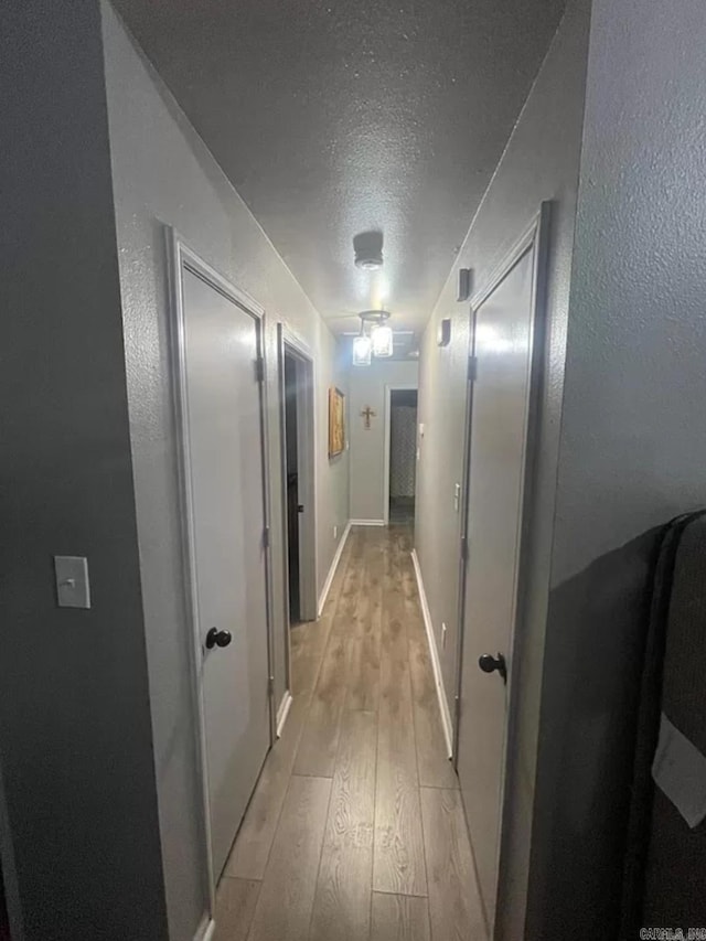 hall with light wood-type flooring and a textured ceiling