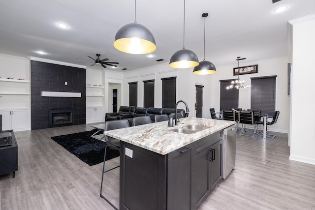 kitchen with a kitchen island with sink, sink, stainless steel dishwasher, built in features, and decorative light fixtures