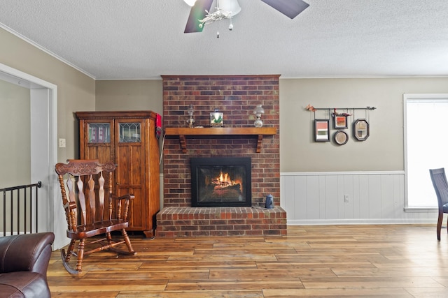 living room with a fireplace, ceiling fan, light hardwood / wood-style flooring, and a textured ceiling